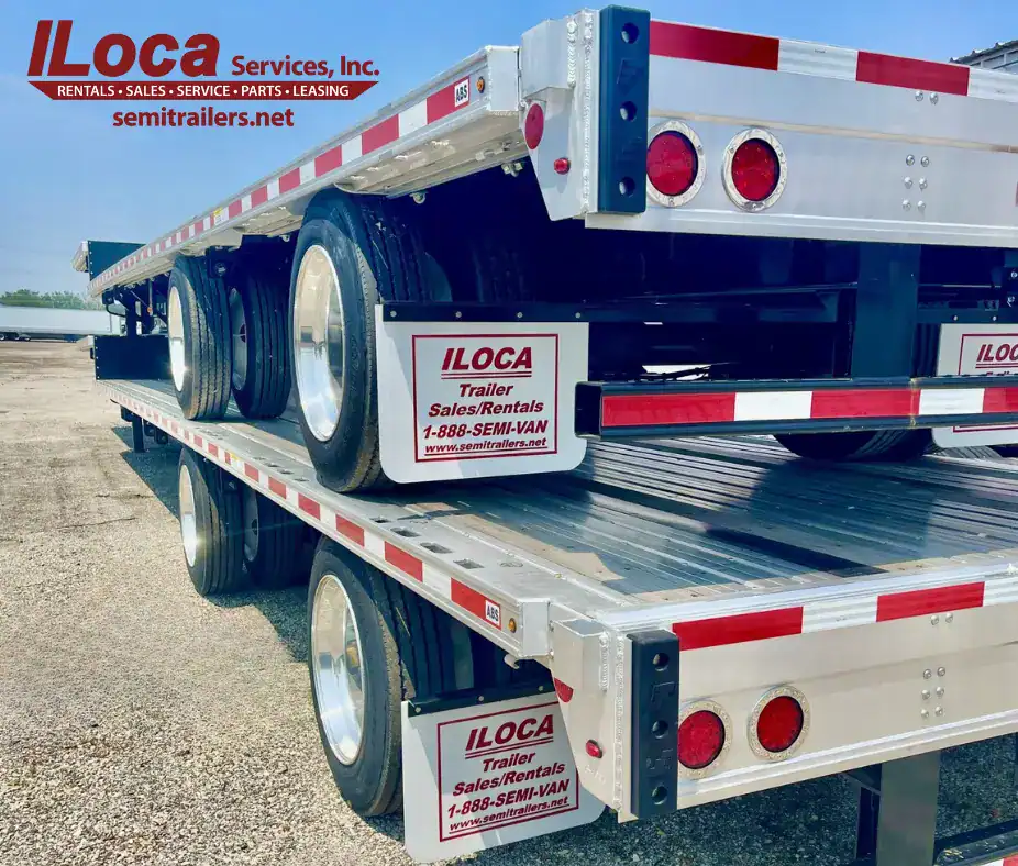 Two white and silver drop-deck semi-trailers stacked on top of each other. The trailers feature red trim, and the mudflaps display the ILoca logo with the text "Trailer Sales/Rentals."